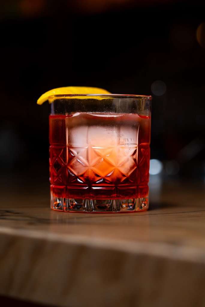 Negroni over a large clear ice cube in a cut-crystal glass with an orange twist