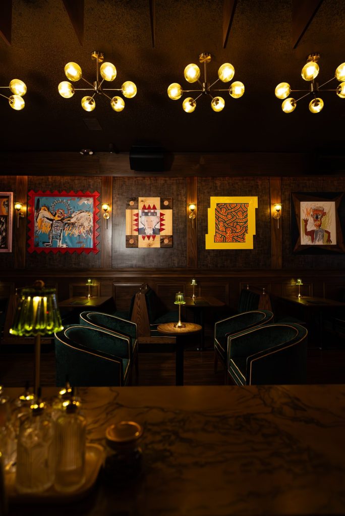 Gallery wall of colorful framed art above lounge seating and green glass lamps