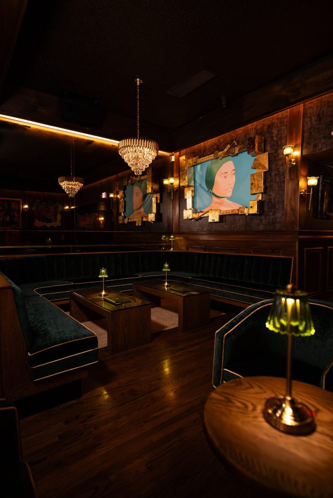 Corner booth in green velvet beneath a crystal chandelier and framed art