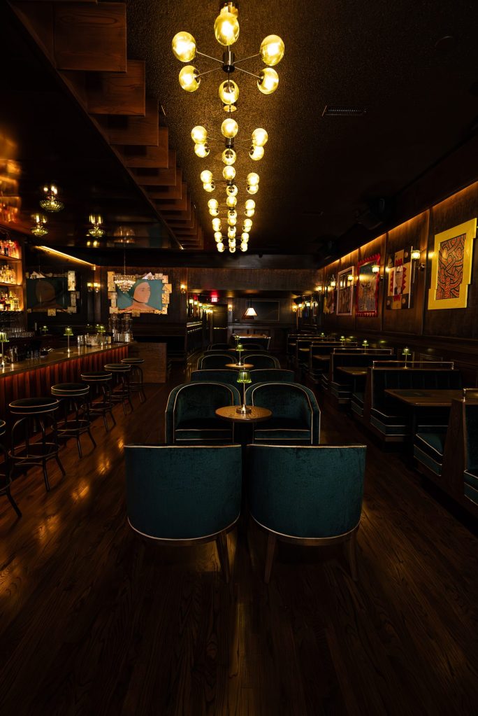 The long room at Ten Cash, with green velvet booths under rows of glowing chandeliers
