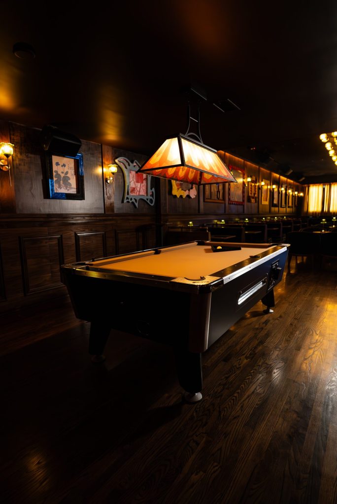 Pool table under a stained-glass lamp in the wood-paneled back room